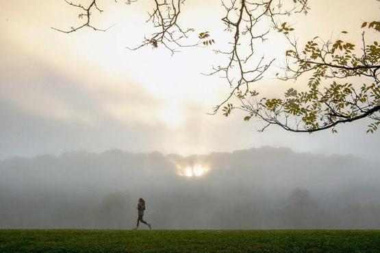 A person runs on the Athens bike path with a sunset peeking through the clouds in the background